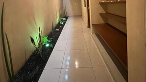 Un pasillo con una fuente de agua negra, suelo de baldosas blancas y una escalera de madera.