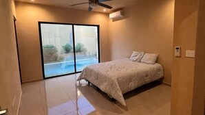 Un dormitorio con cama, ventilador de techo y vista a una piscina a través de un ventanal.