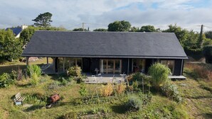 Una casa amb teulada fosca, grans finestres i un porxo cobert amb mobles d'exterior.