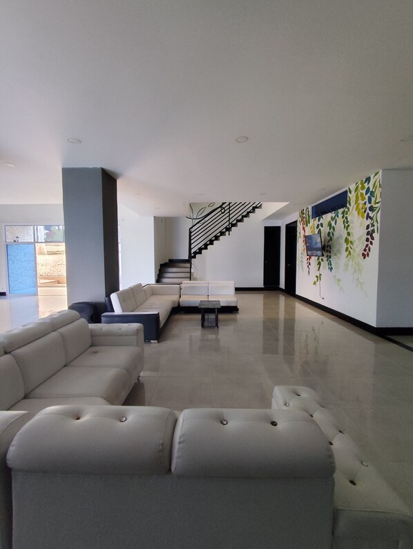 A spacious living area with a modern staircase, a large sectional sofa, and a wall with a leaf pattern. - Finca El Encanto Calima (Calima)