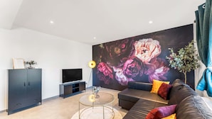 Een moderne woonkamer met een grote bloemenmuur, een ronde glazen salontafel, een leren bank en een donkere kast.