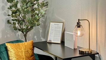 Een kamer met een groene fluwelen bank, een gouden sierkussen, een klein tafeltje met een bord 'welkom', een decoratieve lamp en een pot met een plant.