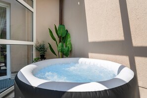 Un jacuzzi inflable lleno de agua, ubicado contra una pared con una ventana y una planta en maceta cerca.