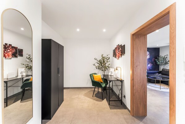 Una sala de estar moderna con un mueble negro, un sillón verde con un cojín amarillo, una mesa de centro redonda y un marco de puerta de madera.