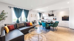 Een moderne woonkamer met een leren bank, een glazen salontafel en een eethoek met turquoise stoelen.
