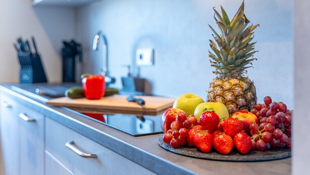 Een keukenblad met een fruitschaal, met onder andere ananas, appels, druiven en aardbeien.