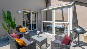 Een terras buiten met rieten meubilair, een barbecue en een glazen deur naar een patio.