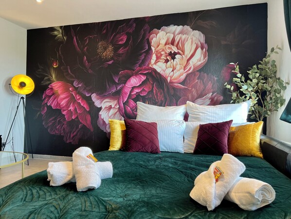 Un dormitorio con un gran mural floral, una colcha verde y varias almohadas.