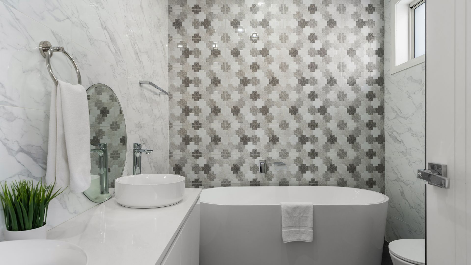 A modern bathroom with a freestanding bathtub, a glass-enclosed shower, and a marble-tiled wall with a geometric pattern.