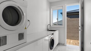 A modern laundry room with a front-loading washer and dryer, a sink, and a window overlooking a brick wall. - Cork & Vine on Coolalta  - A Cellar Door Escape (Nulkaba)
