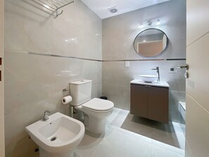 A modern bathroom with a toilet, bidet, sink, and mirror.