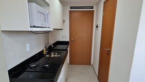 Une cuisine de taille réduite, équipée d’une cuisinière à gaz, d’un four à micro-ondes, d’un évier et d’une porte en bois.