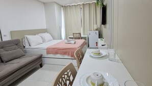 Une chambre d’hôtel moderne équipée d’un lit, d’un canapé, d’une table à manger avec des assiettes et des verres, et d’un téléviseur fixé au mur.
