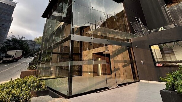 A modern glass building with a geometric design, surrounded by taller buildings. - Loft con Tecn- Alexa (Bogotá)