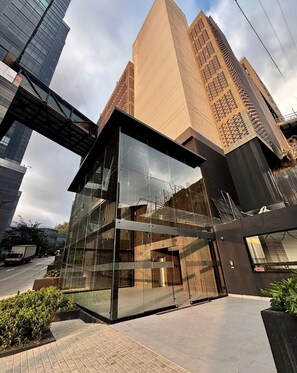 Ein modernes Glasgebäude mit geometrischem Design, umgeben von höheren Gebäuden.