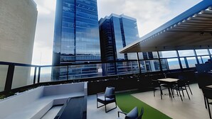 A modern rooftop lounge with a view of tall buildings, seating areas, and a green carpet. - Loft con Tecn- Alexa (Bogotá)
