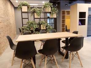 Ein Konferenzraum mit einem langen Tisch, schwarzen Stühlen und einer Ziegelwand. Hinter dem Tisch stehen Pflanzen in Töpfen auf Regalen.