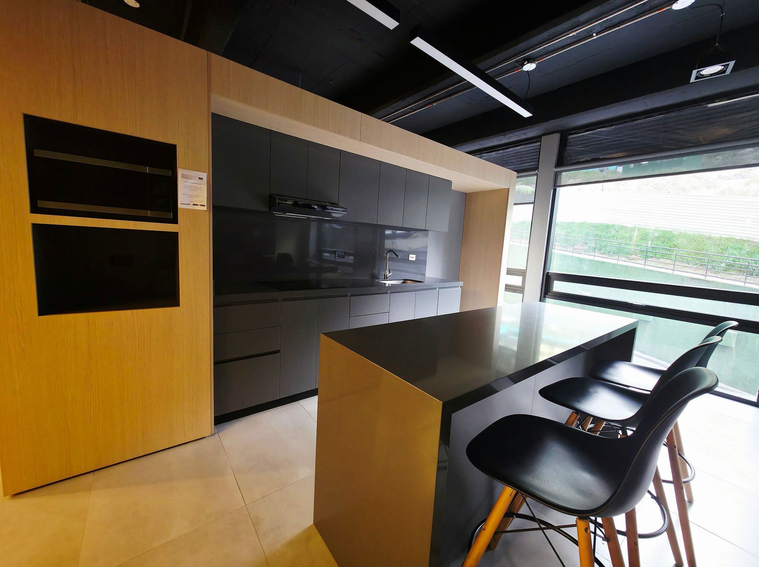 A modern kitchen with a built-in oven, a large island with bar stools, and a view through the window.