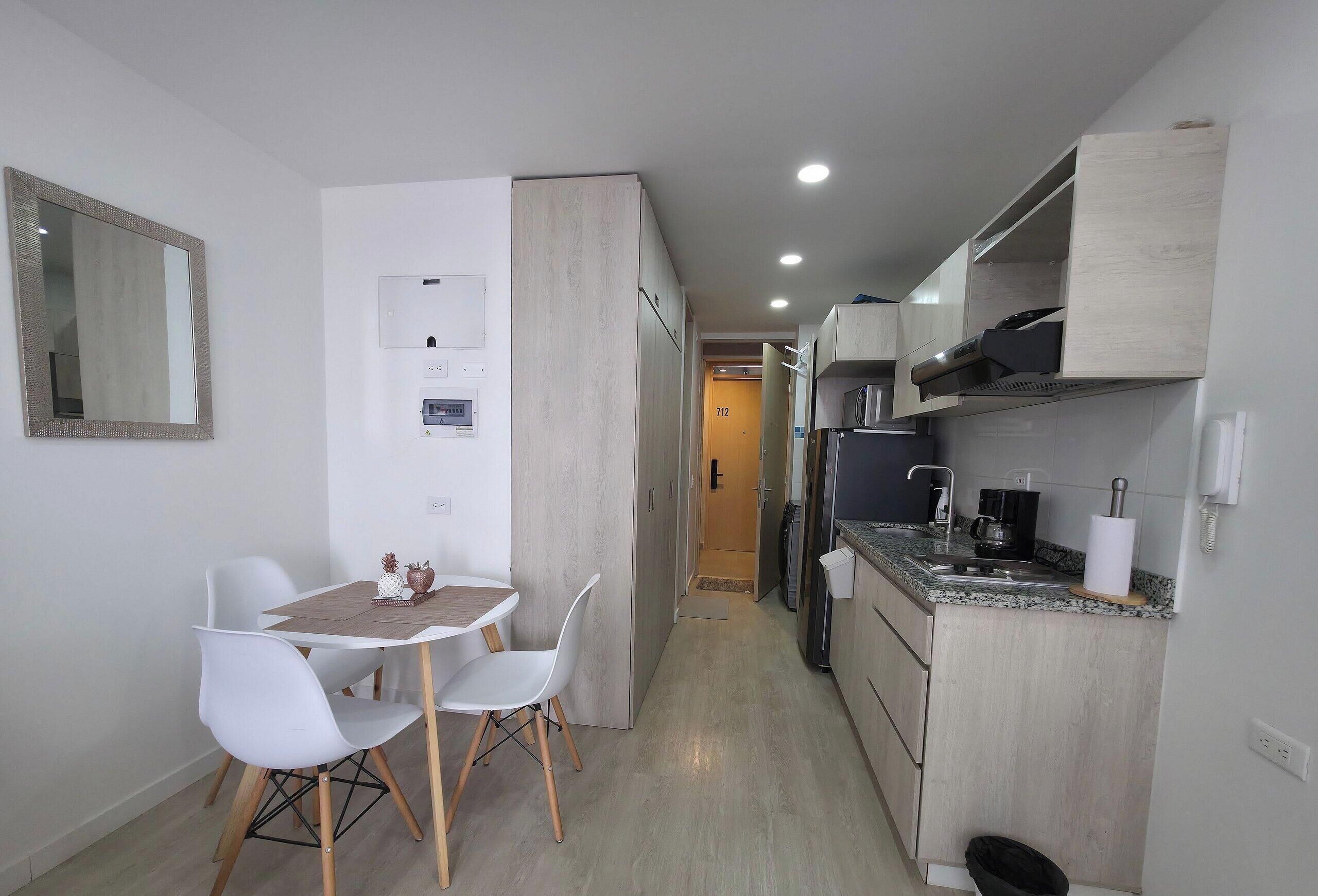 A compact kitchen with a dining area, a microwave, a coffee maker, and a trash bin.