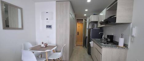 A compact kitchen with a dining area, a microwave, a coffee maker, and a trash bin.