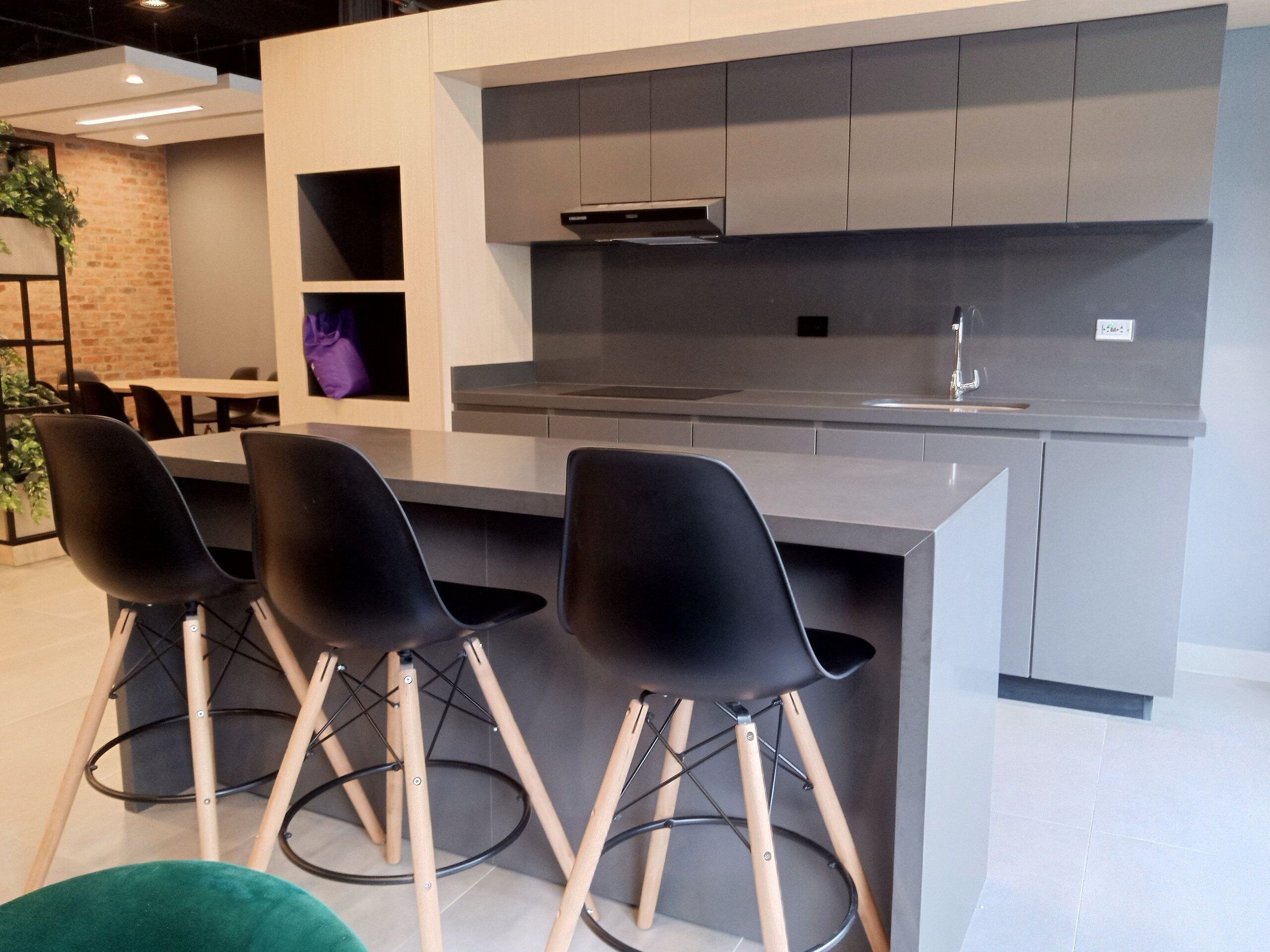 A modern kitchen with grey cabinets, a stainless steel range hood, and three black bar stools with wooden legs.