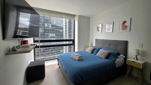 A modern bedroom with a large bed, a TV mounted on the wall, and a window with a city view. - Loft con Tecn- Alexa (Bogotá)