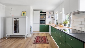 Una cocina moderna con armarios blancos y verdes, piso de madera y alfombra roja.