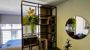 A modern bedroom with a bed, a wooden shelving unit with plants, a round mirror, and a view of the city through the window. - The best apartment in the best area of Bogota (Bogotá)