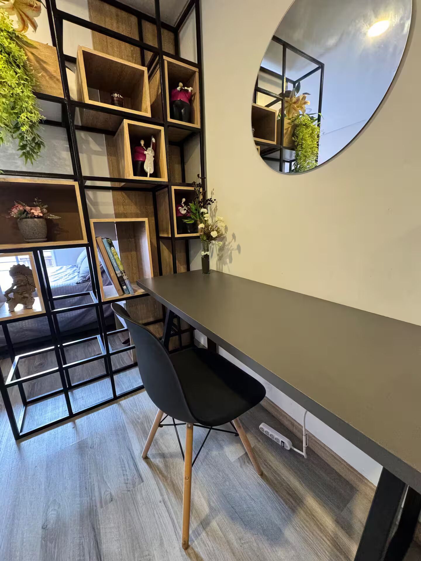 Un espace repas moderne avec une longue table, des chaises noires et des étagères en bois ornées de plantes.