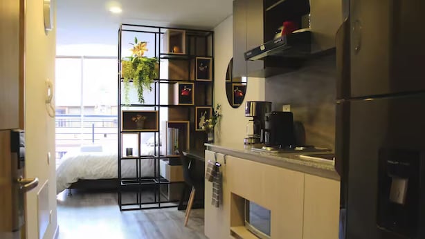 A compact kitchen with a built-in stove, a coffee machine, and a refrigerator. There is a small seating area with a chair and a table. A window provides natural light and a view of the outside. - The best apartment in the best area of Bogota (Bogotá)