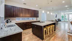 A modern kitchen with dark wood cabinets, a large island with stools, a built-in oven, and a window overlooking the outdoors. - Hermann Park Hideaway Sleeps 12 w/ Parking & Patio (Houston)