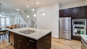 A modern kitchen with a central island, stainless steel appliances, and a staircase leading to another level. - Hermann Park Hideaway Sleeps 12 w/ Parking & Patio (Houston)