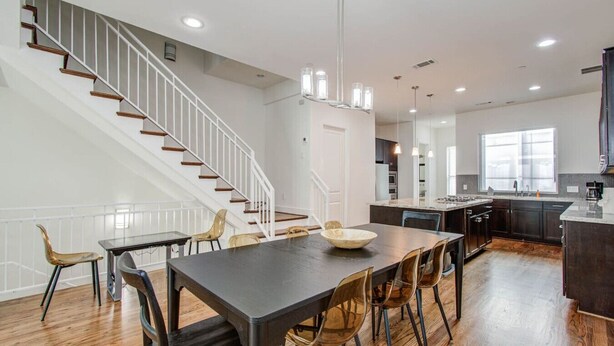 A modern kitchen with a central island, wooden flooring, and a staircase leading to an upper level. - Hermann Park Hideaway Sleeps 12 w/ Parking & Patio (Houston)