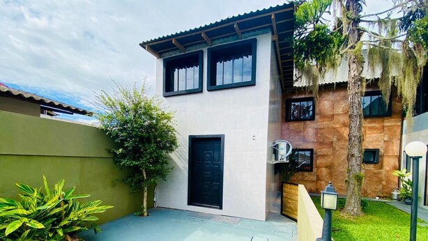 A modern two-story house with a flat roof, a black front door, and a small balcony.