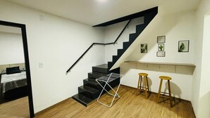 A staircase with black steps and a white handrail, leading to a landing with a shelf and two stools.