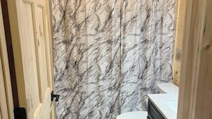 A bathroom with a marble-patterned shower curtain, a white toilet, and wooden cabinets. - Happy Pappys - Store Cabin (Current Township)