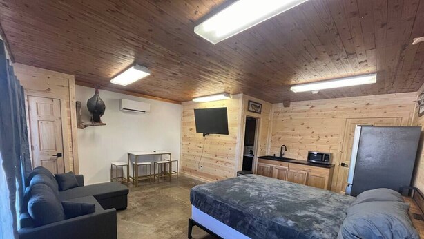 A room with a bed, a sofa, a small kitchen area, and a TV mounted on the wall. - Happy Pappys - Store Cabin (Current Township)