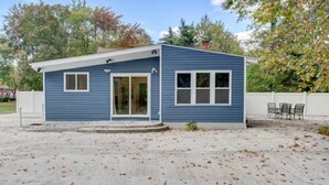 A small, single-story house with a blue exterior, a front door, and a patio area with chairs.