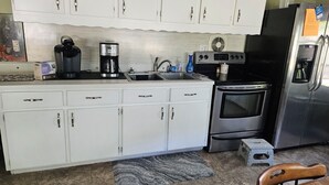 Una cocina con armarios blancos, estufa, fregadero y refrigerador.