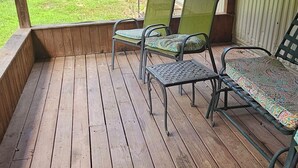 Una terraza de madera con sillas y una mesa de metal, con vista a un jardín césped y una casa con garaje.