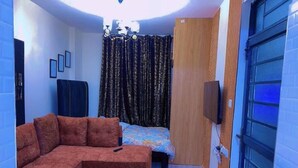A compact room with a sofa, a bed, a TV, and a curtain. - G1 Studio with a lift,balcony &underground parking (Nairobi)