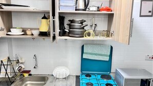 A compact kitchen with a blue gas stove, a microwave, and a sink. - G1 Studio with a lift,balcony &underground parking (Nairobi)