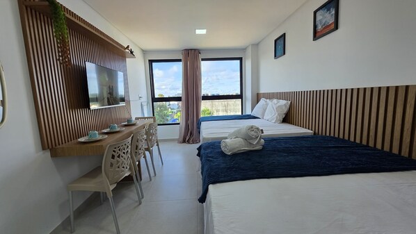 A hotel room with a bed, a desk with chairs, a TV, and a window with a view. - Flat Porto de galinha Villas 311 byLP (Ipojuca)