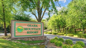 Señal de Ozark Mountain Resort rodeada de exuberante vegetación y árboles.