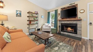Una sala de estar acogedora con chimenea, un televisor montado encima y un sofá cómodo.