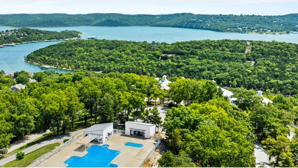 Vista aérea de un resort con piscina, rodeado de bosque denso y un lago.