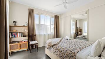 A bedroom with a bed, a bookshelf, a chair, a ceiling fan, and a large mirror.