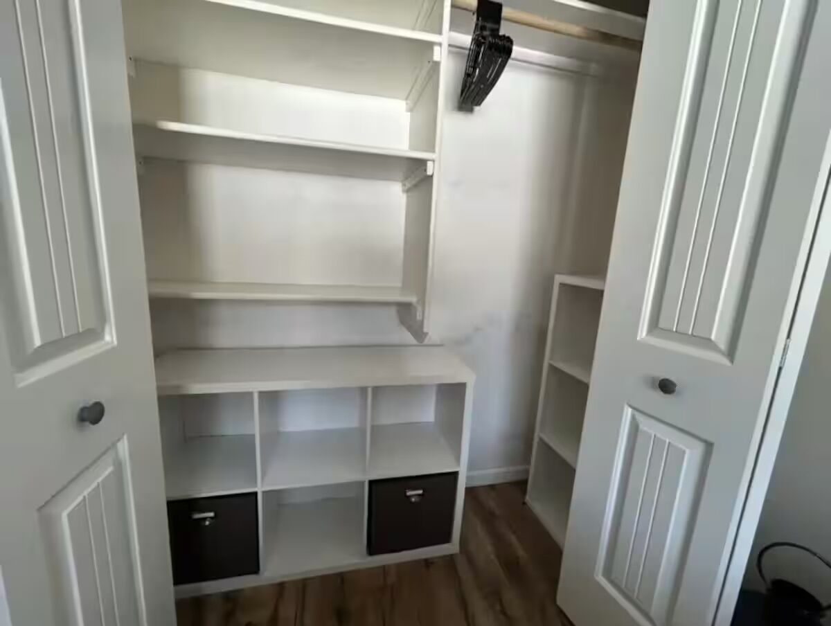 A walk-in closet with multiple shelves and drawers, white doors, and a wooden floor.