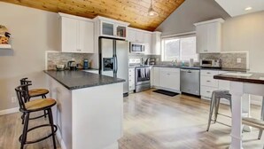 Une cuisine moderne avec des meubles blancs, un îlot central, des appareils en acier inoxydable et un plafond en bois.