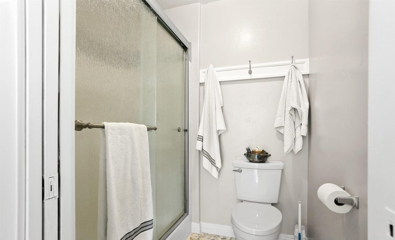 A bathroom with a glass shower door, a toilet, and a towel rack with multiple towels.